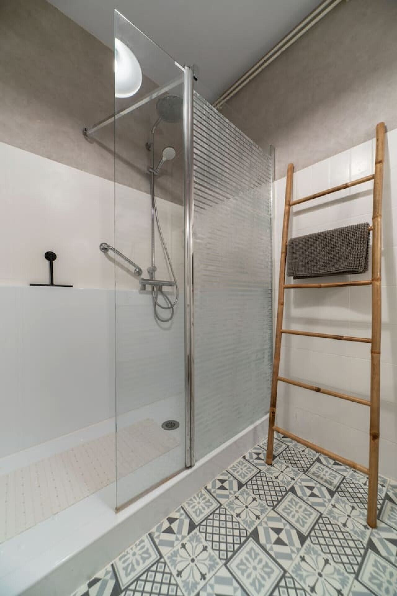 Un box de ducha moderno con puerta de cristal, una escalera de madera y baldosas de suelo estampadas.