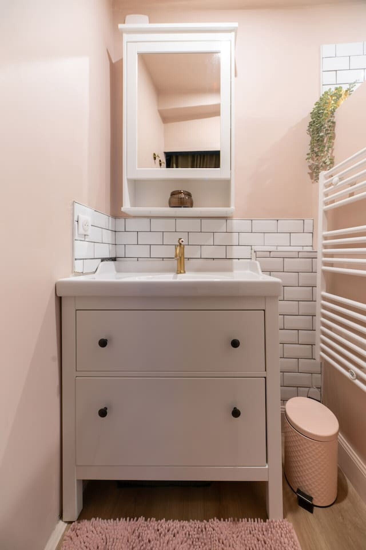 A bathroom with a white sink, a mirror above it, and a small trash bin.