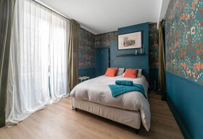A bedroom with a bed, curtains, and a wall with floral wallpaper. - Grande Maison Cusset - 5 rue Fourneris - Cusset (Cusset)