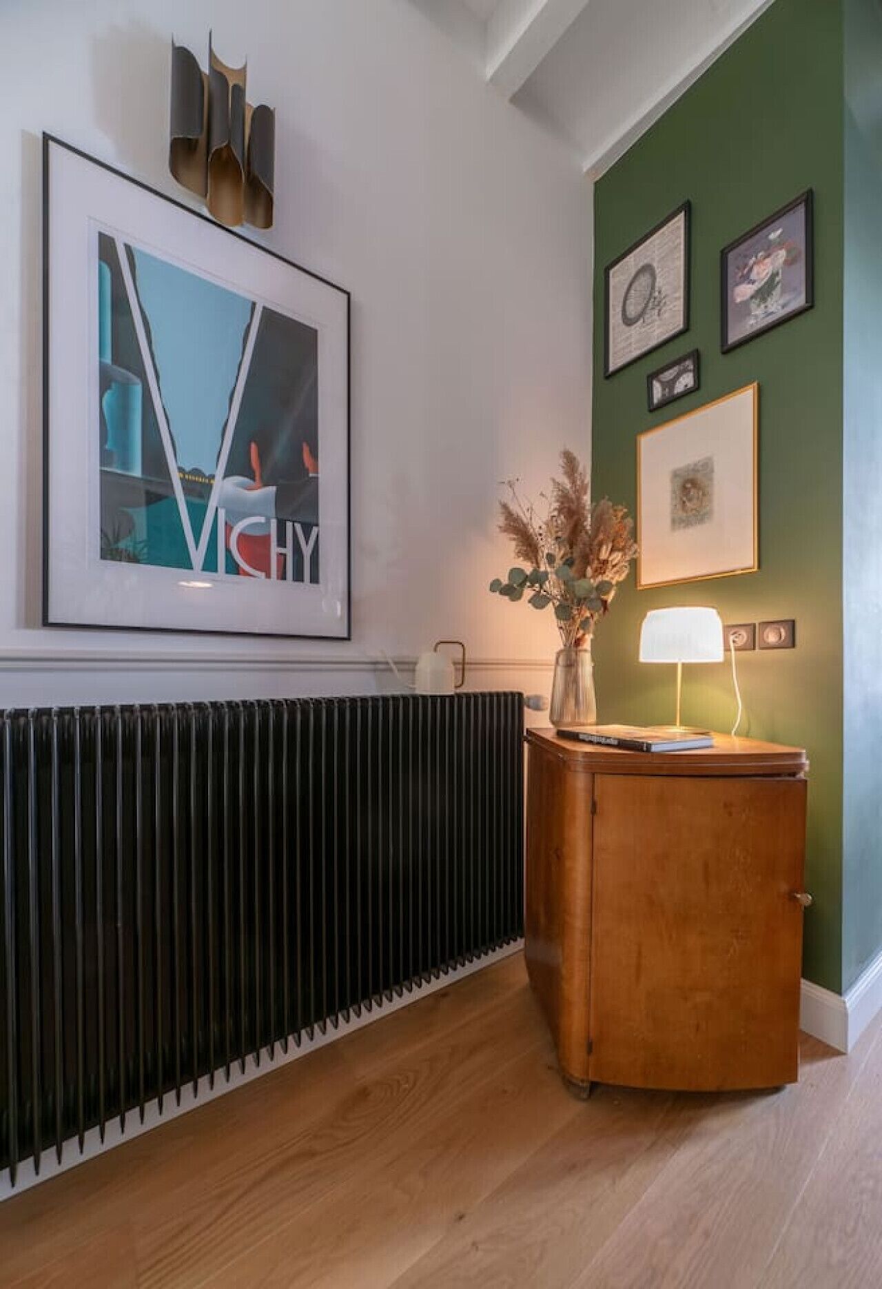 Ein Zimmer mit Heizkörper, einem Holzschrank mit Lampe und gerahmten Bildern an der Wand.