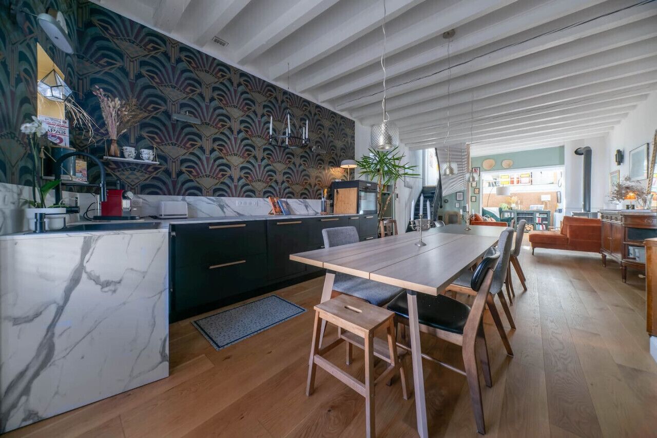 Eine moderne Küche mit Marmorarbeitsplatte, einem Essbereich mit Holztisch und -stühlen sowie einer Wandverkleidung mit Muster-Tapete.