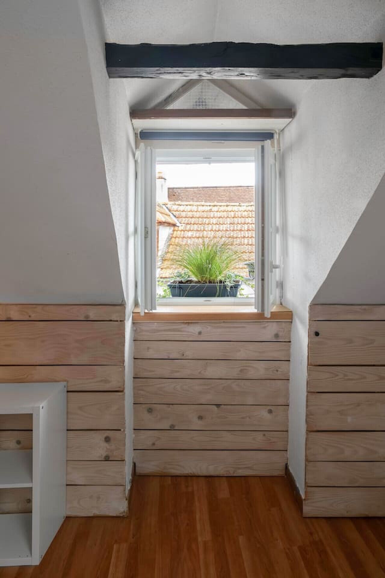 Ein kleines Zimmer im Dachgeschoss mit schrägen Wänden, Holzboden und einem Fenster mit Blick auf einen Garten.