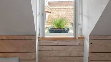 Ein kleines Zimmer im Dachgeschoss mit schrägen Wänden, Holzboden und einem Fenster mit Blick auf einen Garten.