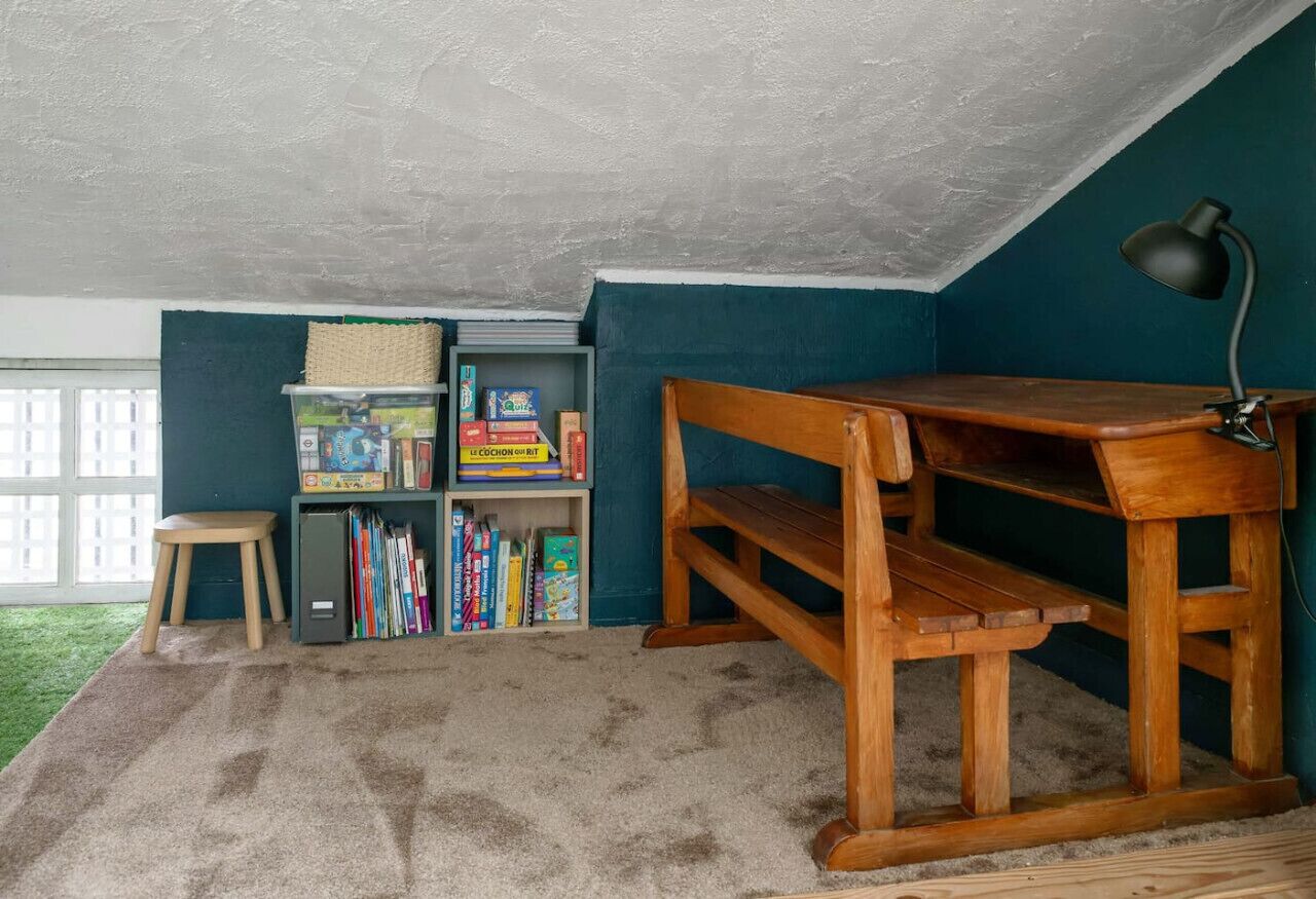 Una habitación con un escritorio de madera, una estantería y una ventana.
