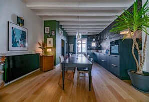 A dining area with a wooden table and chairs, a green accent wall, and a kitchen with dark cabinets and a tiled backsplash. - Grande Maison Cusset - 5 rue Fourneris - Cusset (Cusset)