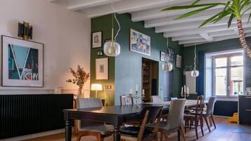 A dining area with a wooden table and chairs, a large potted plant, and a ceiling with exposed beams.