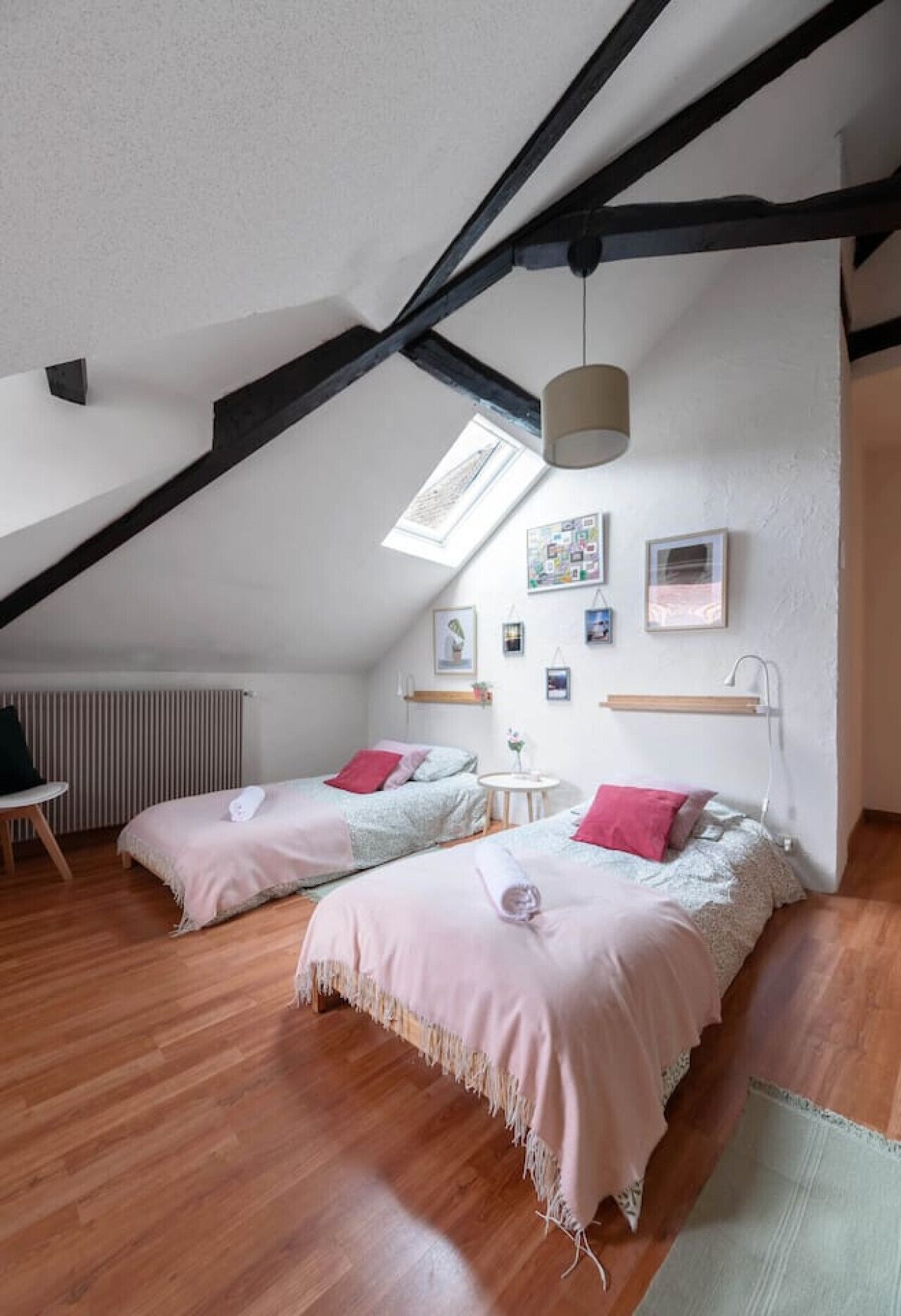 Une chambre confortable située sous les toits, avec deux lits, un plancher en bois, une lucarne et une petite table ronde.