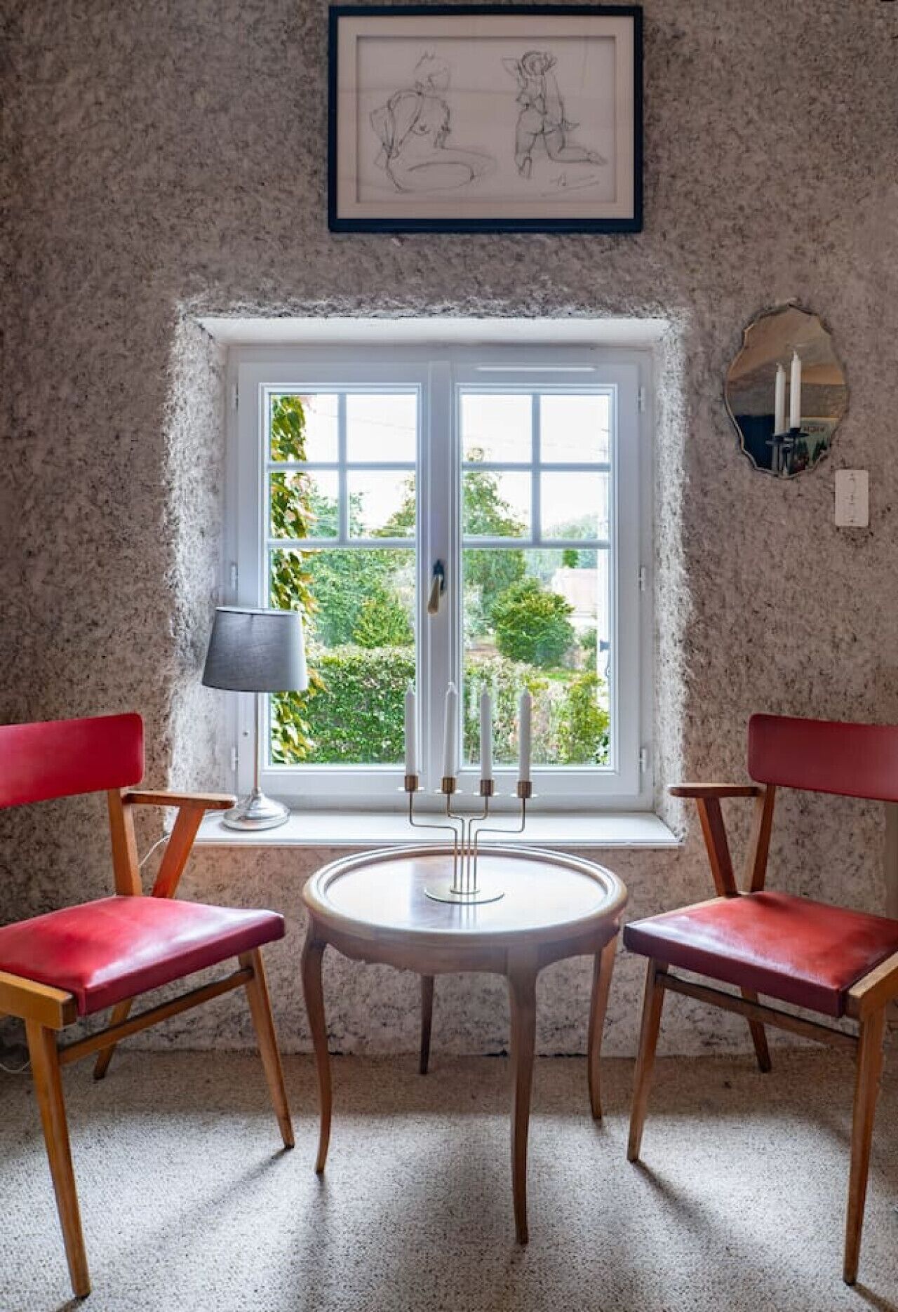 Una habitación con un ventanal grande, una mesa con candelabro y dos sillas rojas.