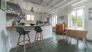 A kitchen with a wooden island, two green chairs, a wooden table, and a hanging light fixture. - Grande Maison design, terrasse, jardin, parking (Creuzier-le-Neuf)