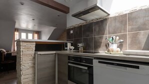 A modern kitchen with a stone accent wall, built-in appliances, and a skylight. - Charmant 2 pièces Centre Ville (Vichy)