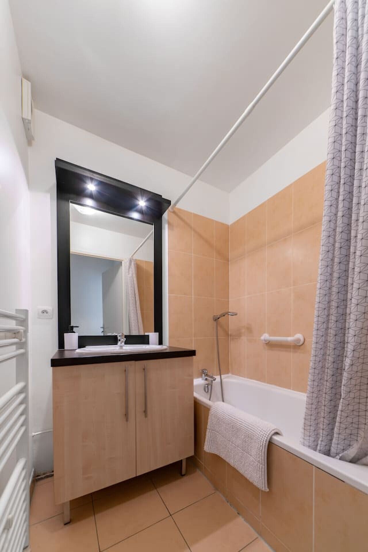 A bathroom with a bathtub, a shower, a vanity with a mirror, and a towel hanging on the wall.