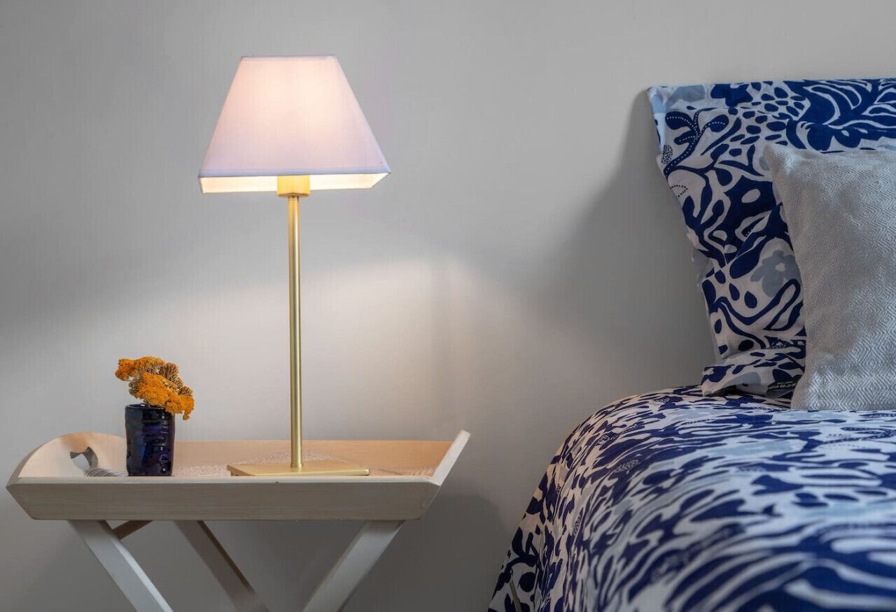 A bedside table with a lamp, a vase with flowers, and a patterned bedspread.