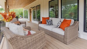 A covered porch with wicker furniture, large windows, and a view of greenery. - Ramsay's Happy Place - River Access & tubes/New Construction (Wimberley)