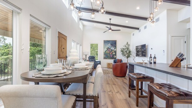 A modern kitchen with a central island, wooden flooring, pendant lighting, and a large window overlooking greenery. - Ramsay's Happy Place - River Access & tubes/New Construction (Wimberley)