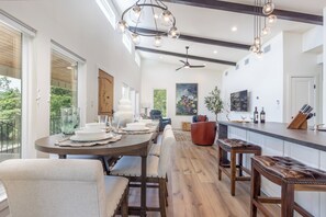 Une cuisine moderne dotée d’un îlot central, de planchers en bois, de luminaires suspendus et d’une grande fenêtre donnant sur un espace verdoyant.