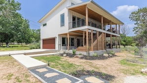 A two-story house with a covered porch, a garage, and a landscaped front yard with a gravel pathway. - Ramsay's Happy Place - River Access & tubes/New Construction (Wimberley)