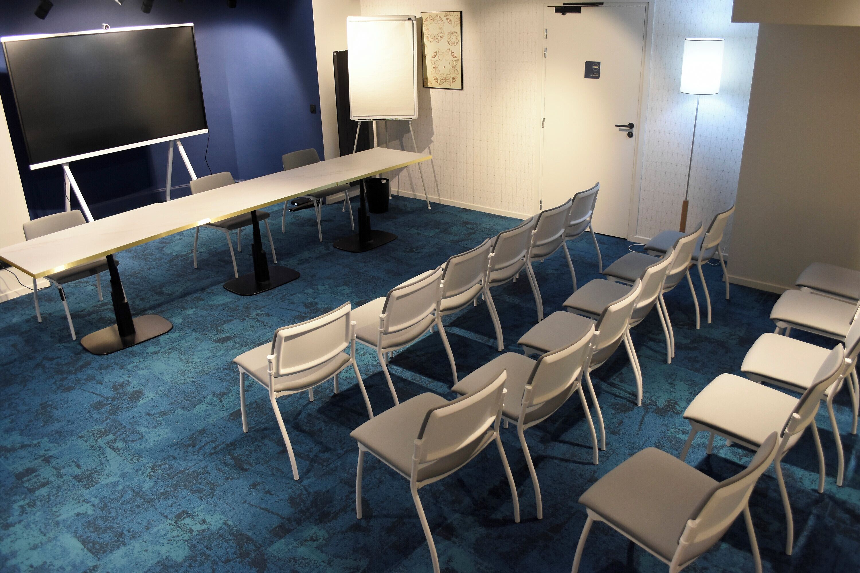 Une salle de conférence équipée d’une longue table, de chaises, d’un tableau blanc et d’un écran de projection.