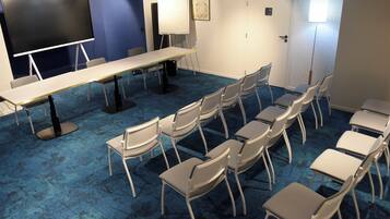 Une salle de conférence équipée d’une longue table, de chaises, d’un tableau blanc et d’un écran de projection.