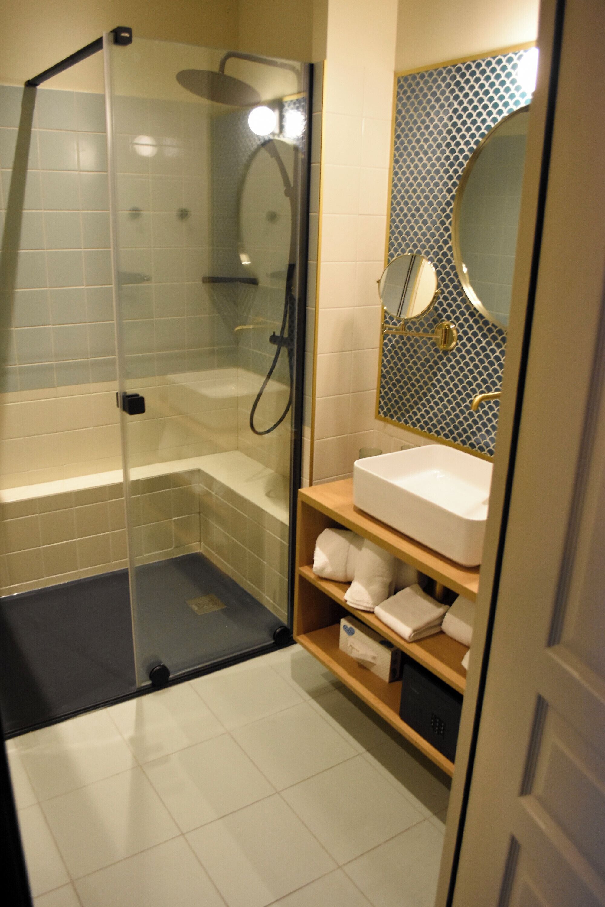 Un bagno moderno con doccia vetro, lavandino bianco e specchio con pannello decorativo in piastrelle.