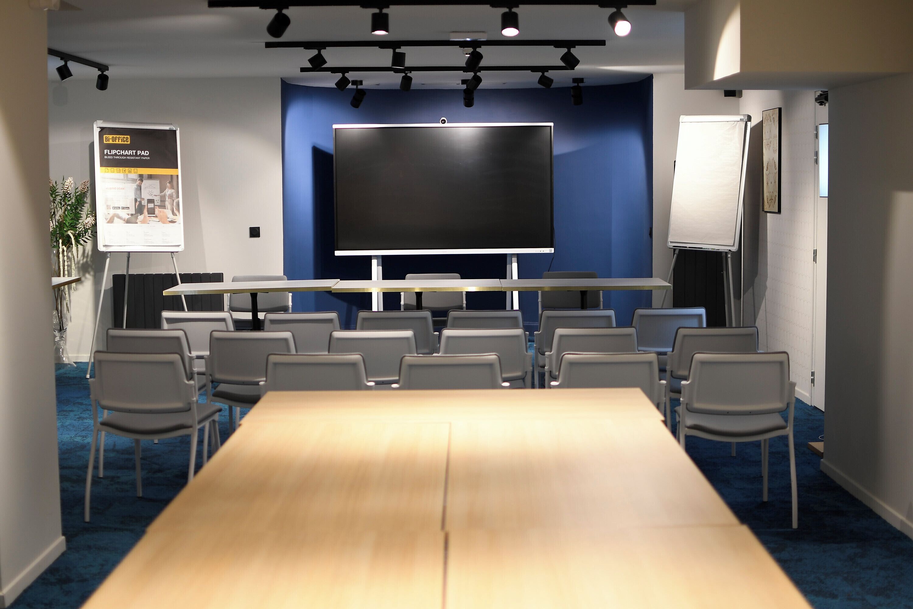 A conference room with a large table, chairs, a flipchart stand, a whiteboard, and a projector screen.