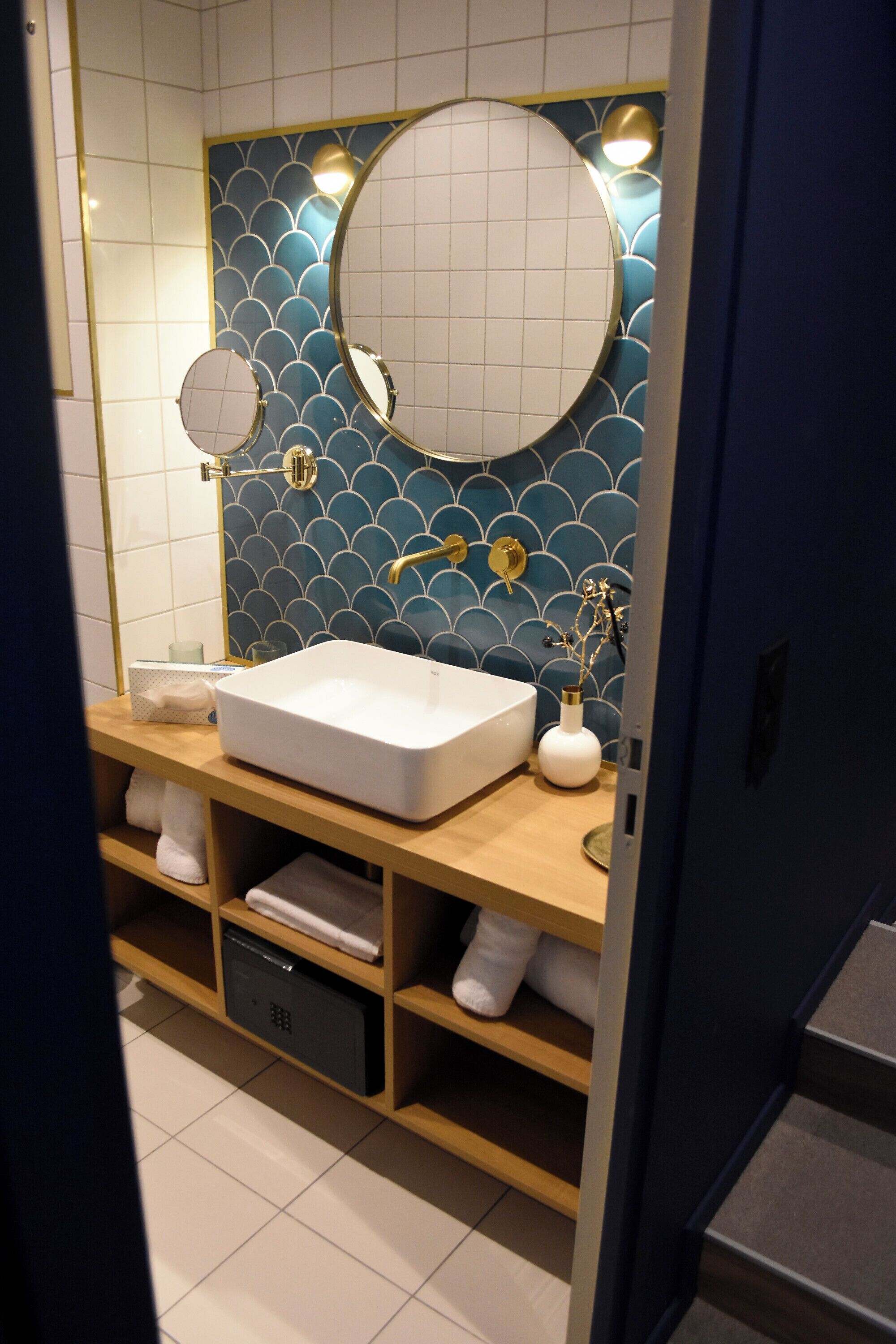 A modern bathroom with a white sink, two mirrors, and a blue tiled wall.