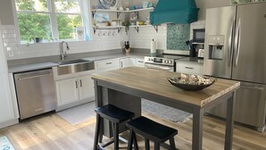 A modern kitchen with white cabinets, a wooden island, stainless steel appliances, and a teal hood.