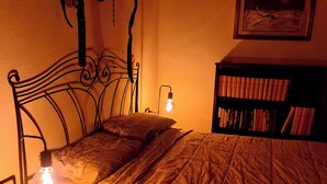 Une pièce faiblement éclairée, avec un lit, une table de chevet, une lampe et une bibliothèque.