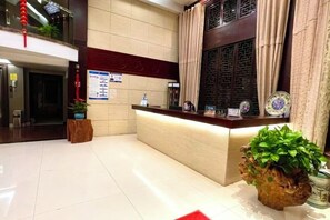 A hotel reception area with a reception desk, a wooden chair, a potted plant, and a window with curtains. - Leinuobinguna (Yueqing)