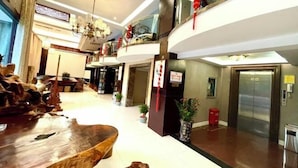 A hotel lobby with a wooden reception desk, a chandelier, potted plants, and an elevator. - Leinuobinguna (Yueqing)