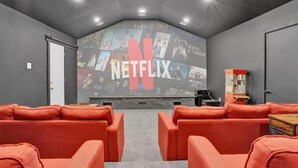 A cozy room with a large wall-mounted screen displaying the Netflix logo, surrounded by red seating.