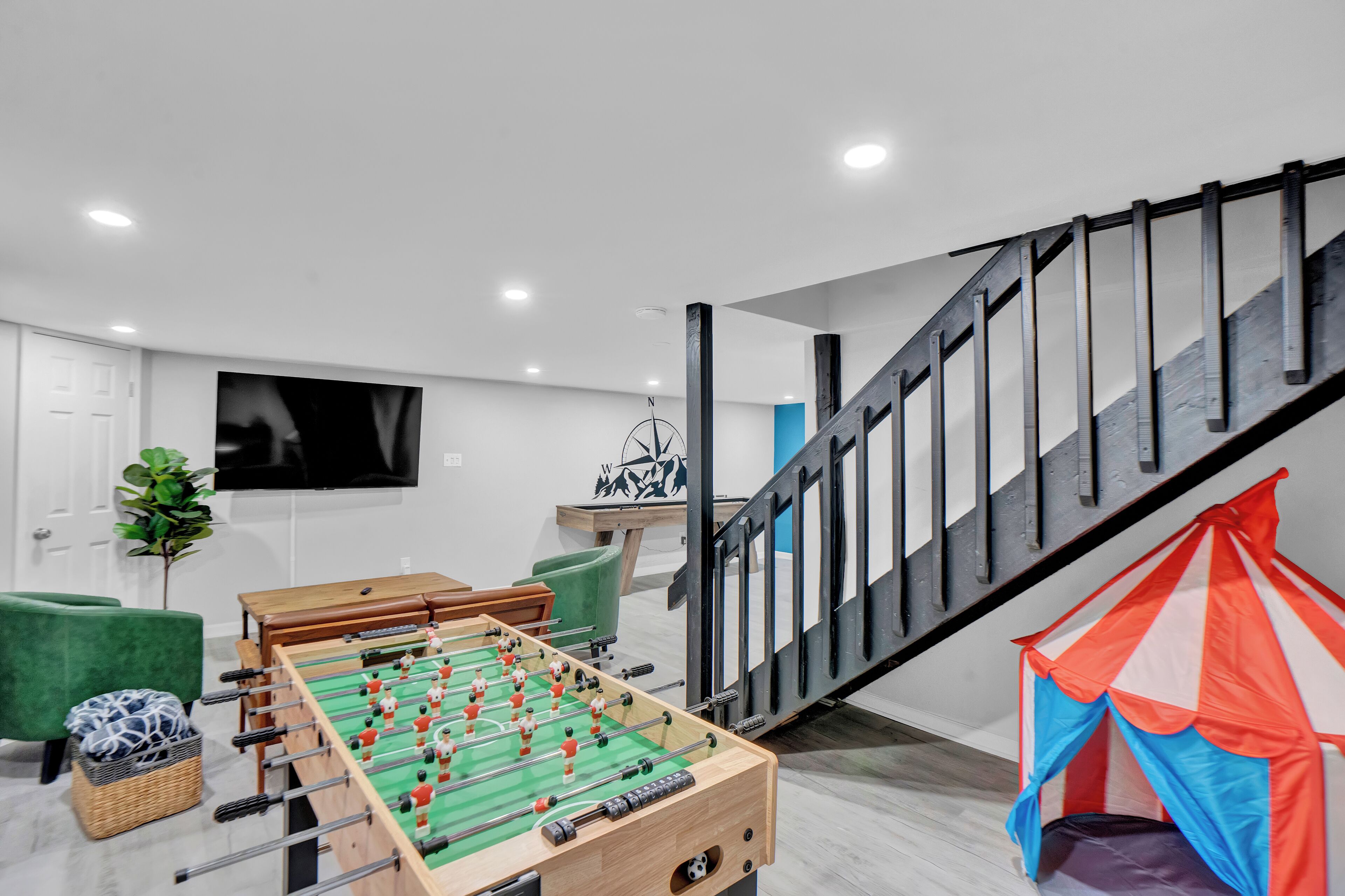 Een moderne woonkamer met een tafelvoetbalspel, een televisie en een trap.