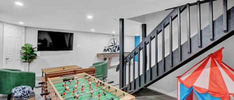 Een moderne woonkamer met een tafelvoetbalspel, een televisie en een trap.