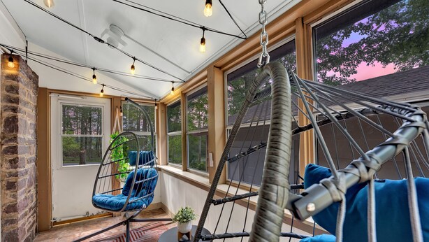 A cozy room with a hanging chair, a hammock, and a view of trees through large windows.