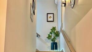 Un escalier en bois avec une rampe, une plante en pot et des œuvres d’art encadrées accrochées aux murs.