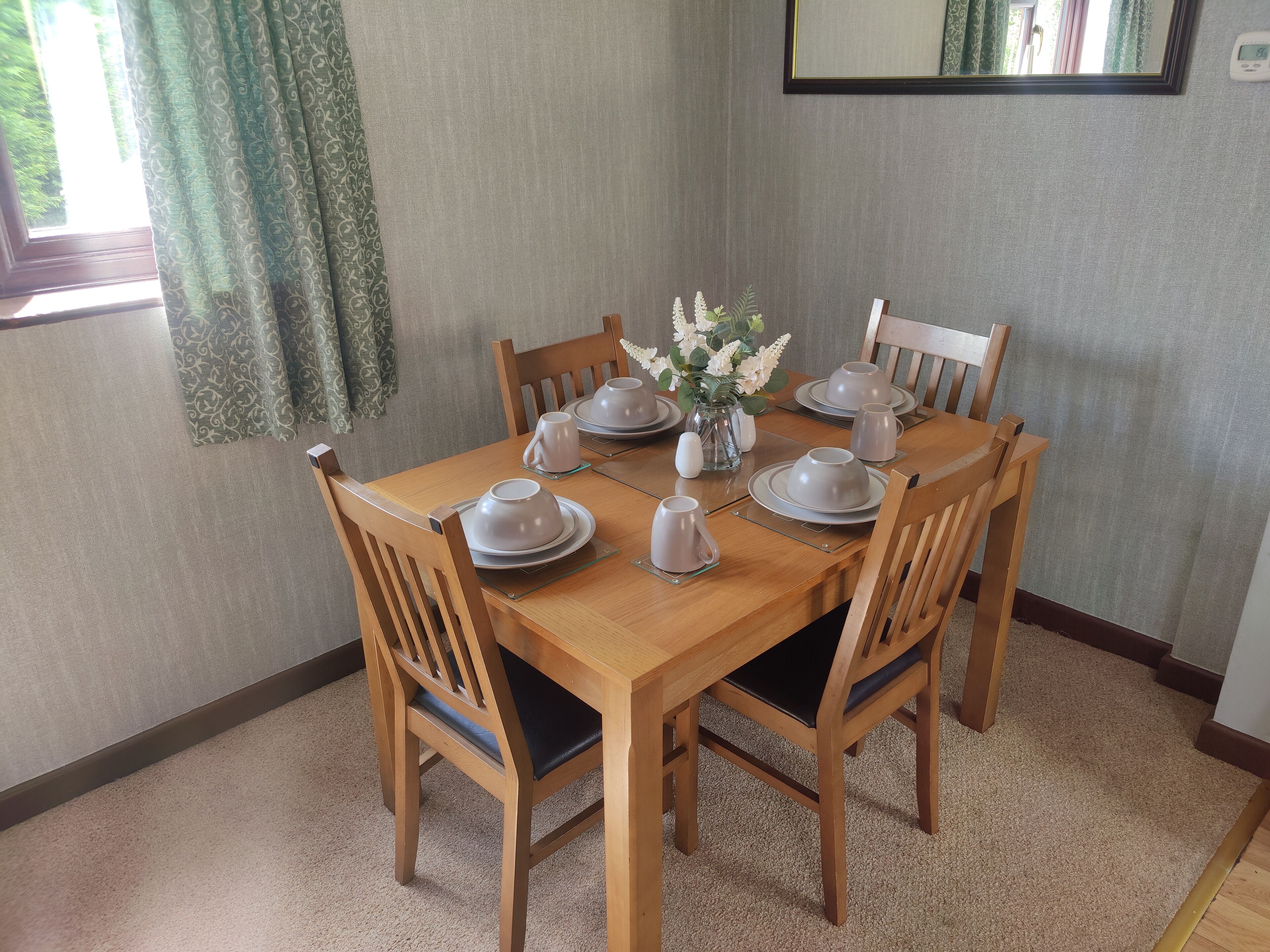 Une table à manger dressée avec des assiettes, des bols et des tasses, entourée de chaises en bois.