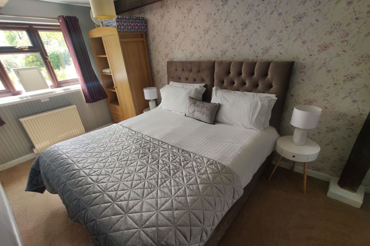 Quarto com uma cama grande, um guarda-roupa, um radiador e uma janela com cortinas.