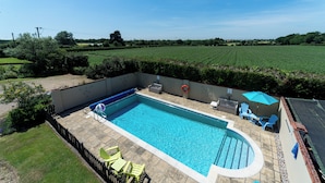 Una piscina rectangular con un borde de baldosas, rodeada por un muro de ladrillo bajo. Hay varias sillas de descanso y una mesa con sombrilla.