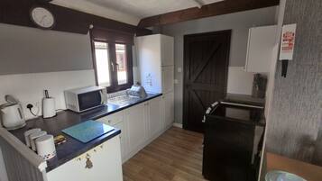 Eine kleine Küche mit Mikrowelle, Toaster und Spüle. Ein Holztür und ein Fenster mit Jalousien sind vorhanden.