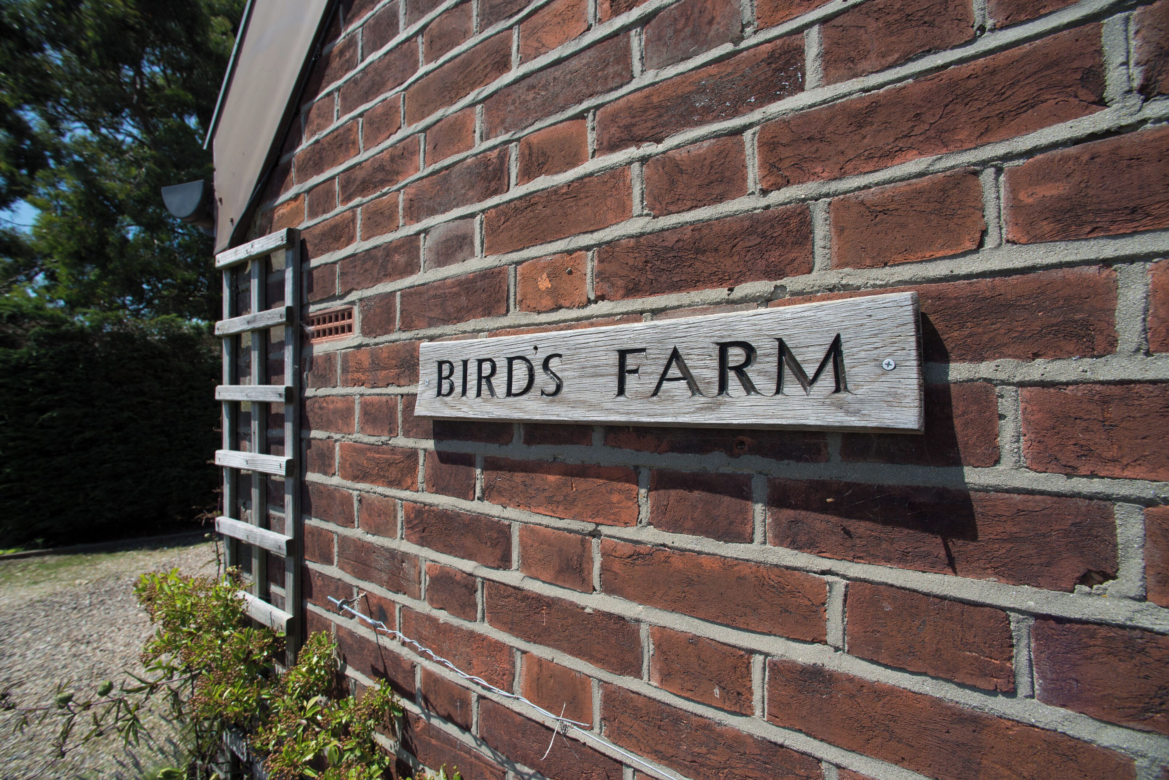 Una pared de ladrillo con un letrero de madera que dice "BIRD'S FARM".