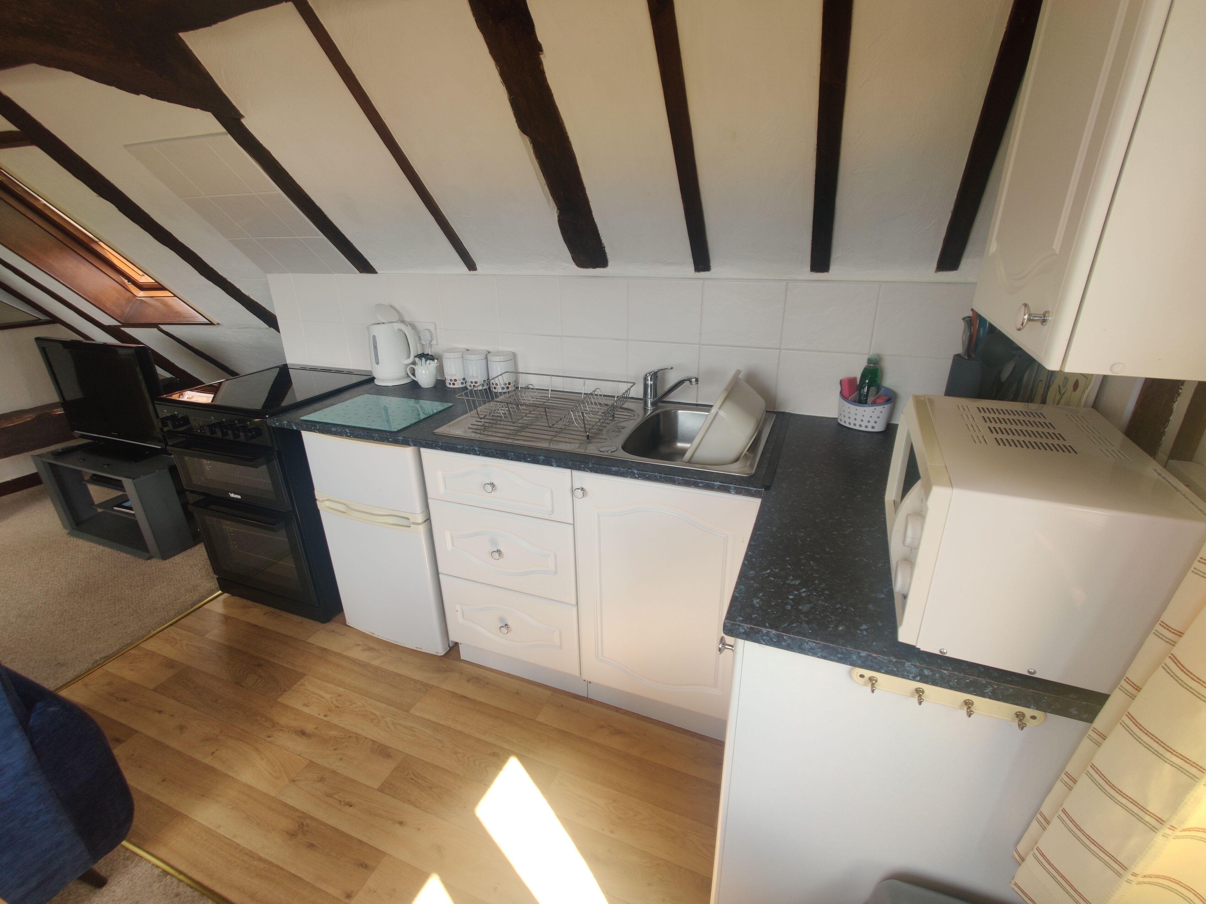 Una cucina compatta con un piano di lavoro nero, mobili bianchi e pavimento in legno.