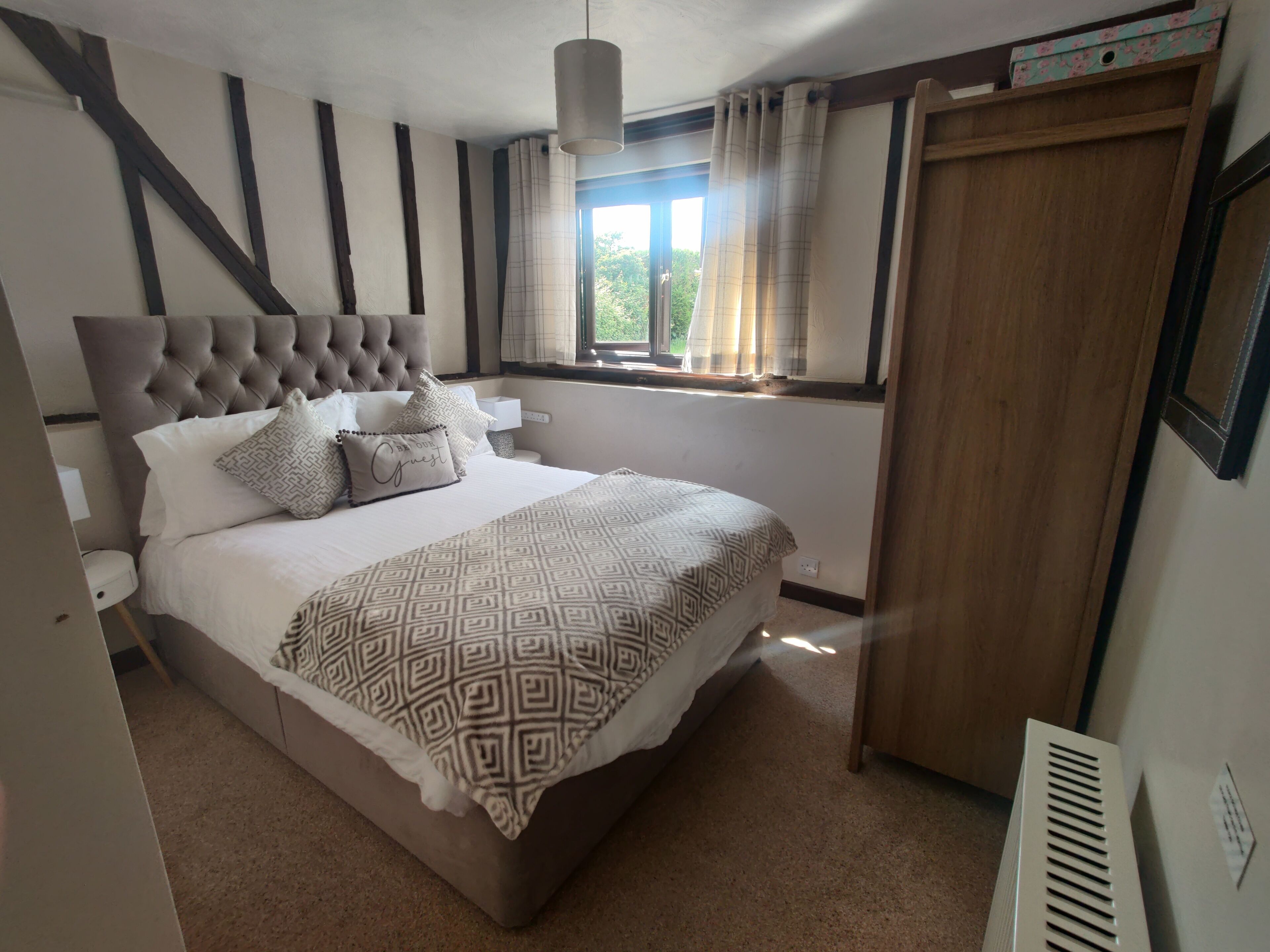 A bedroom with a large bed, a window with curtains, a wooden headboard, and a radiator.