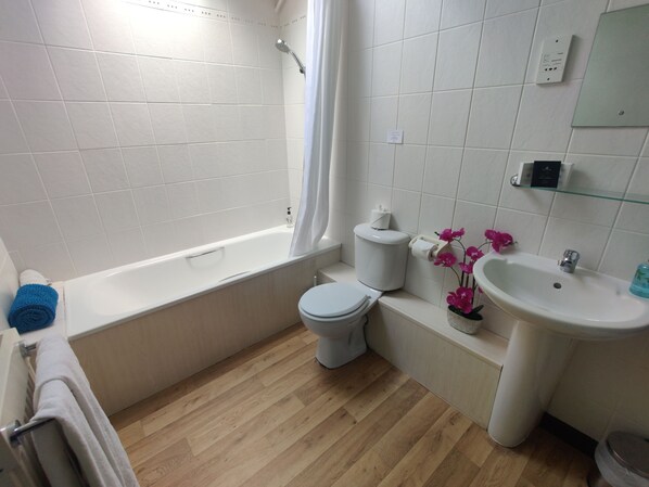 A bathroom with a bathtub, toilet, sink, and a shower curtain. - Birds Farm (Colchester)