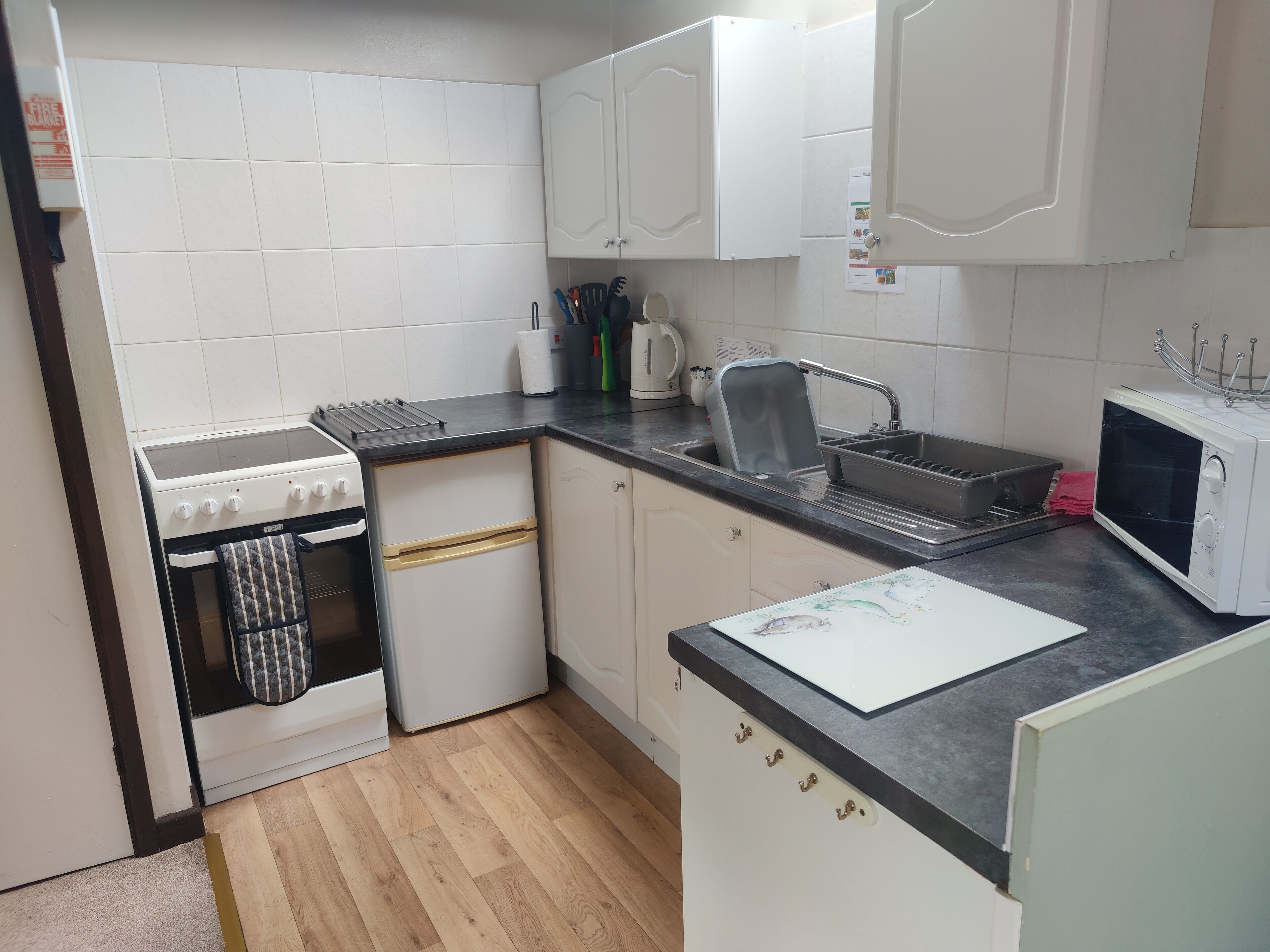 A compact kitchen with white cabinets, a stove, a sink, and a microwave.