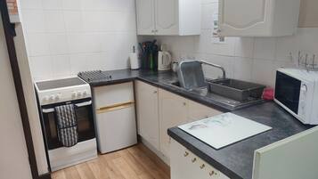 A compact kitchen with white cabinets, a stove, a sink, and a microwave.