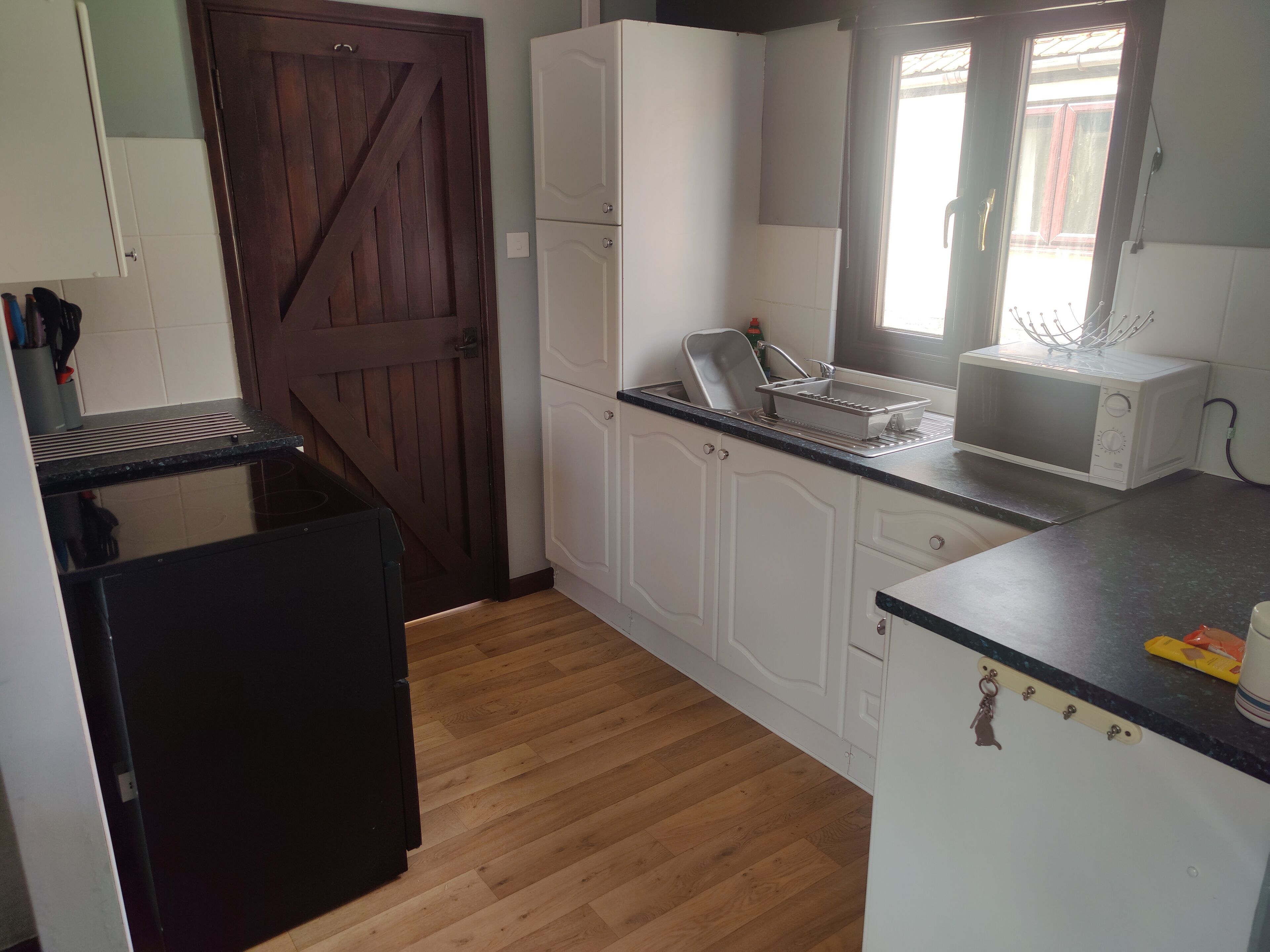 Una cocina compacta con armarios blancos, una puerta de madera, un microondas y un lavamanos.