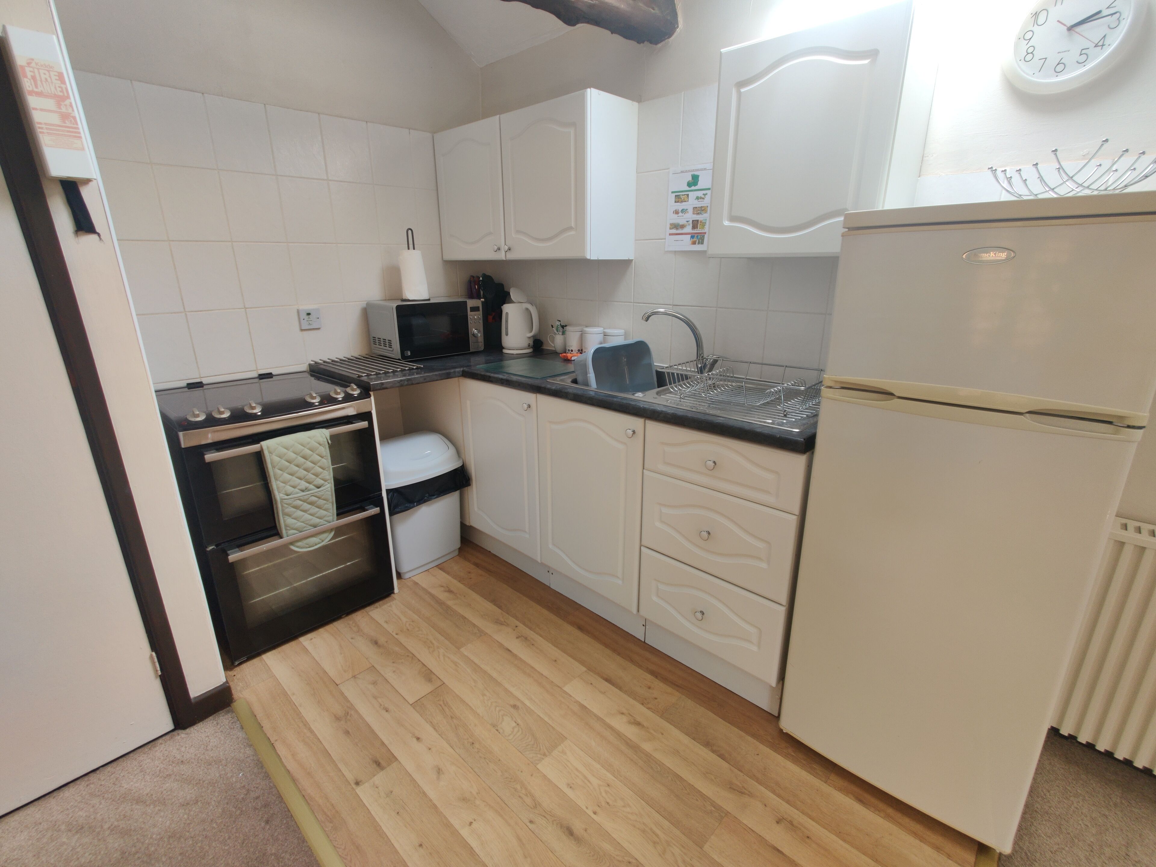Une cuisine de taille réduite avec des meubles blancs, un four à micro-ondes, une cuisinière et un réfrigérateur.