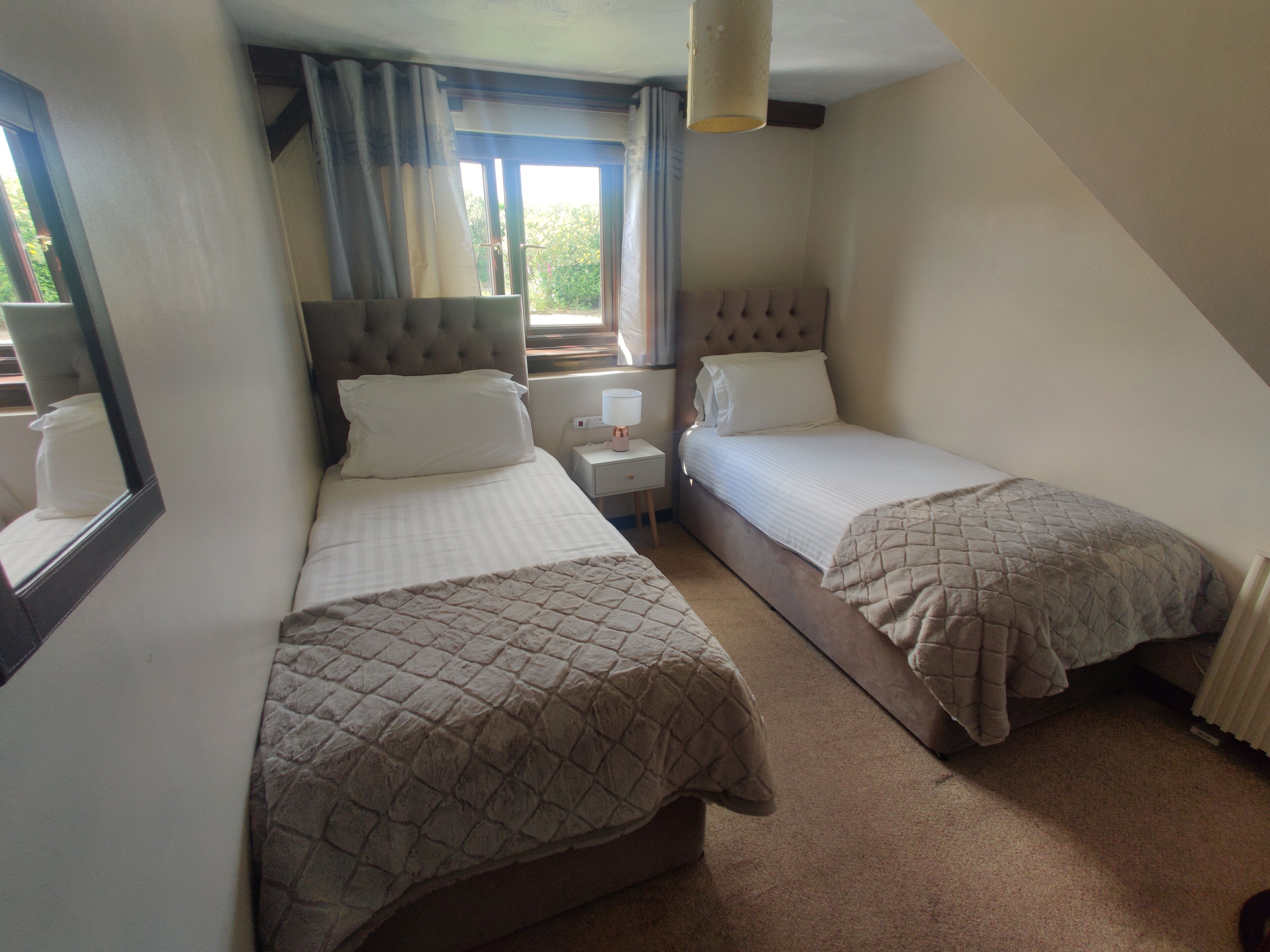 A bedroom with two single beds, a nightstand, a lamp, and a window with curtains.