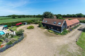 A large house with a gravel driveway, a swimming pool, and a garden with various plants and flowers. - Birds Farm (Colchester)