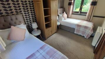 A bedroom with two beds, a wardrobe, a bedside table with a lamp, and a window with curtains.