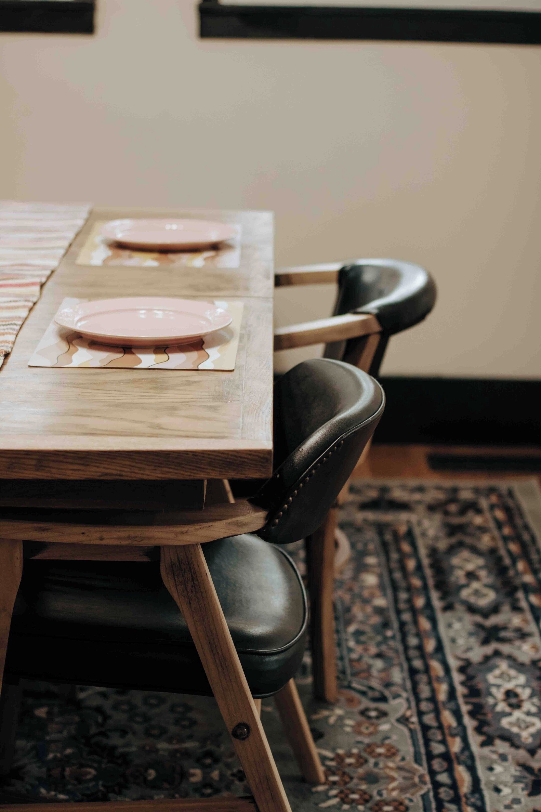 A wooden dining table with two pink plates and black leather chairs.
